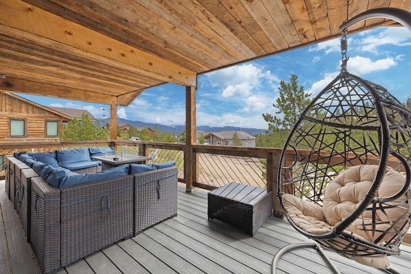 A covered outdoor deck with wicker furniture, a hanging chair, and a view of mountains.
