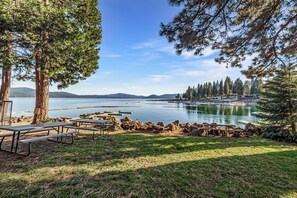 A lakeside picnic area with picnic tables and a bench, surrounded by trees and a view of the lake.