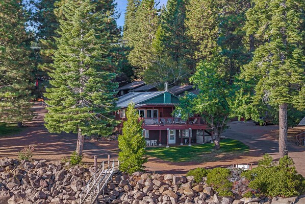 A lodge with a deck, surrounded by trees and a stone wall.