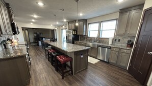 A modern kitchen with a central island, bar stools, stainless steel appliances, and a large window providing natural light.