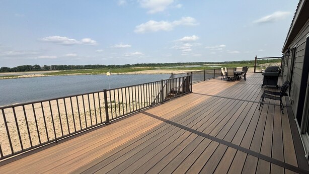 A wooden deck with a railing overlooking a body of water, a barbecue grill, and outdoor seating.