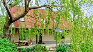 Ein Haus mit rotem Ziegeldach, umgeben von üppigem Grün und einem großen Baum.
