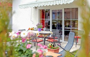 En terrasse med et bord, stole, en potteplante og et vindue med gardiner.