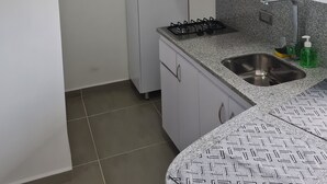 A compact kitchen with white cabinets, a gas stove, a stainless steel sink, and a granite countertop. - 407 Moderno Aparta-Suite en Versalles Tipo Loft - Cali Tower Suites & Lofts (Cali)
