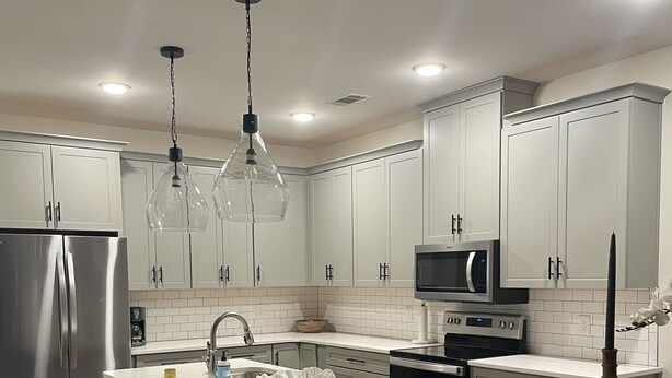 Cocina moderna con armarios blancos, electrodomésticos de acero inoxidable, una isla central con taburetes e iluminación colgante.