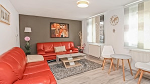 A modern living room with a red sofa, a glass coffee table, and a white dining area. - Ferienhaus Röbel/Müritz (Röbel/Müritz)