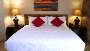 A hotel room with a large bed, two nightstands with lamps, a painting of a sunset, and a wooden headboard. - SUMMER DISCOUNT-- 10% discount on the room rate for Aug. Sept. Just ask Barb. (Kihei)