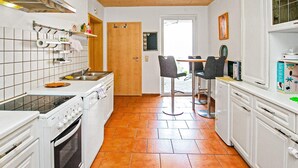 Una cocina compacta con armarios blancos, una estufa y un fregadero. Hay una zona de comedor con dos sillas y una mesa.