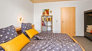 Un dormitorio con una cama que tiene una colcha con estampado de estrellas, dos almohadas, una estantería con libros y un cuadro, y una puerta de madera.