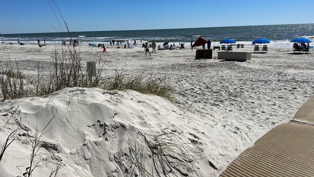 Une plage avec des dunes de sable, des chaises de plage, des parasols et quelques personnes.