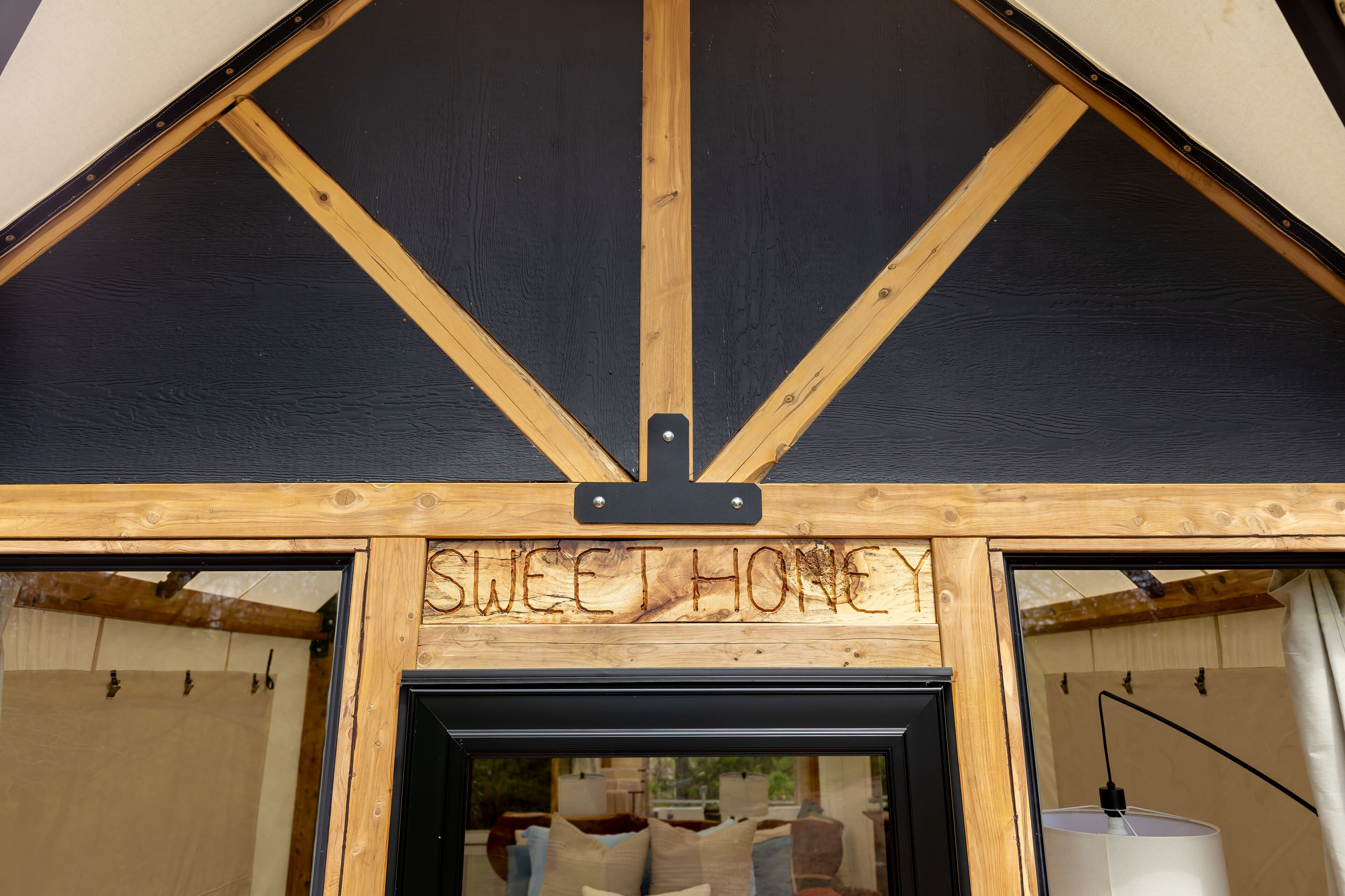 Een houten constructie met een bord waarop 'SWEET HONEY' staat, en een uitzicht op een kamer met een bed en een lamp.