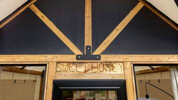 Een houten constructie met een bord waarop 'SWEET HONEY' staat, en een uitzicht op een kamer met een bed en een lamp.