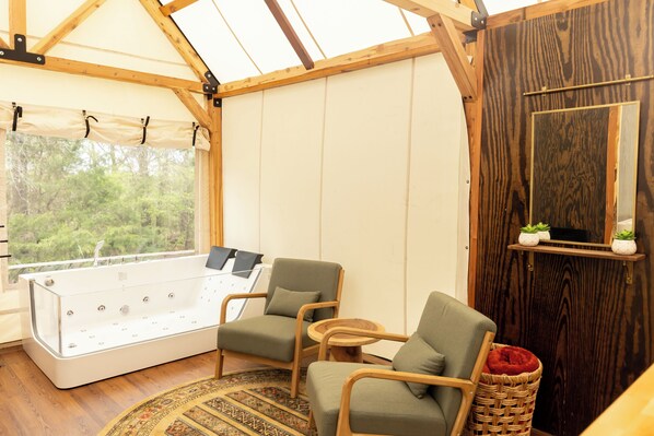 A cozy room with a wooden ceiling, a large window, a bathtub, and two chairs.