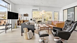 Un salon spacieux doté d’un grand téléviseur, de sièges confortables et offrant une vue sur l’extérieur.