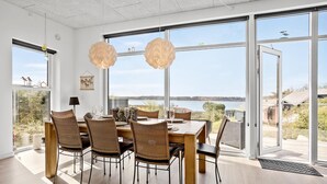 Un espace repas avec vue sur la mer, de grandes fenêtres et des chaises en osier.