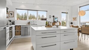 Une cuisine moderne avec des meubles blancs, un lave-vaisselle encastré et un grand îlot central doté de tiroirs.