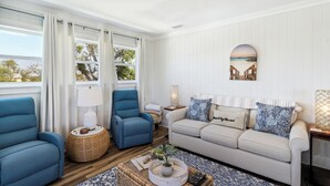 Un salón con sofá, dos sillones, una mesa de centro y vistas al exterior a través de amplios ventanales.