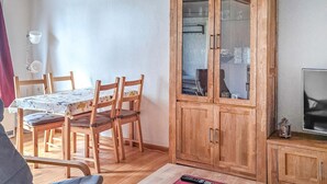 Uma área de refeições com uma mesa e cadeiras de madeira, um armário com portas de vidro e uma televisão em um suporte.