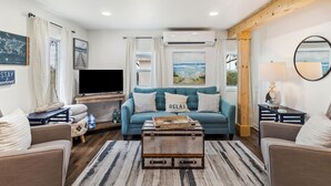 A living room with a blue sofa, a wooden chest, and a television. - "Recuperation Cottage" offers gulf views and is steps to the beach! Pet-friendly, boat parking (Port Saint Joe)
