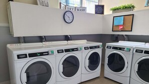 A laundry facility with four Maytag washing machines, a clock, and a sign indicating 'FOLD DRY WASH' above the machines. - Ground Level Ocean View Cottage - Breathtaking Ocean Views -D7 North Coast Village (Oceanside)