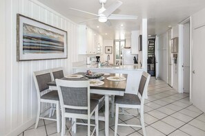 A dining area with a table and chairs, a ceiling fan, and a kitchen in the background.