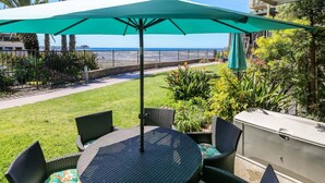 An outdoor patio with a table and chairs, a green umbrella, and a view of the ocean. - Ground Level Ocean View Cottage - Breathtaking Ocean Views -D7 North Coast Village (Oceanside)