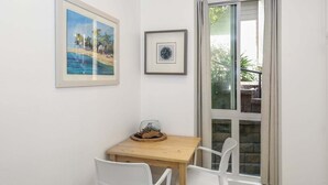 A small dining area with a wooden table and two white chairs, a framed painting, and a framed abstract art piece on the wall. - Ground Level Ocean View Cottage - Breathtaking Ocean Views -D7 North Coast Village (Oceanside)