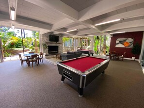 A pool table, a sofa, a fireplace, and a dining area with chairs.