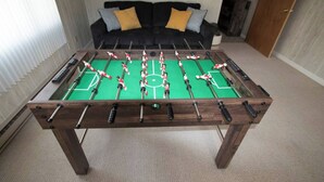 A foosball table in a room with a sofa and cushions in the background. - All Season Fully Furnished Home (Waskish)