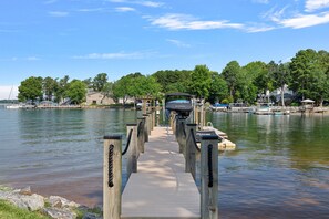 A wooden pier leading to a dock with boats and a house in the background.