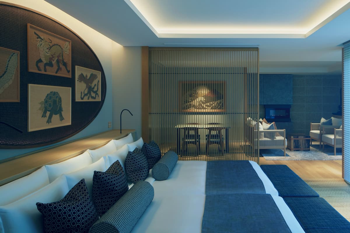 A modern bedroom with a large bed, a dining area, and a seating area with sofas and chairs.