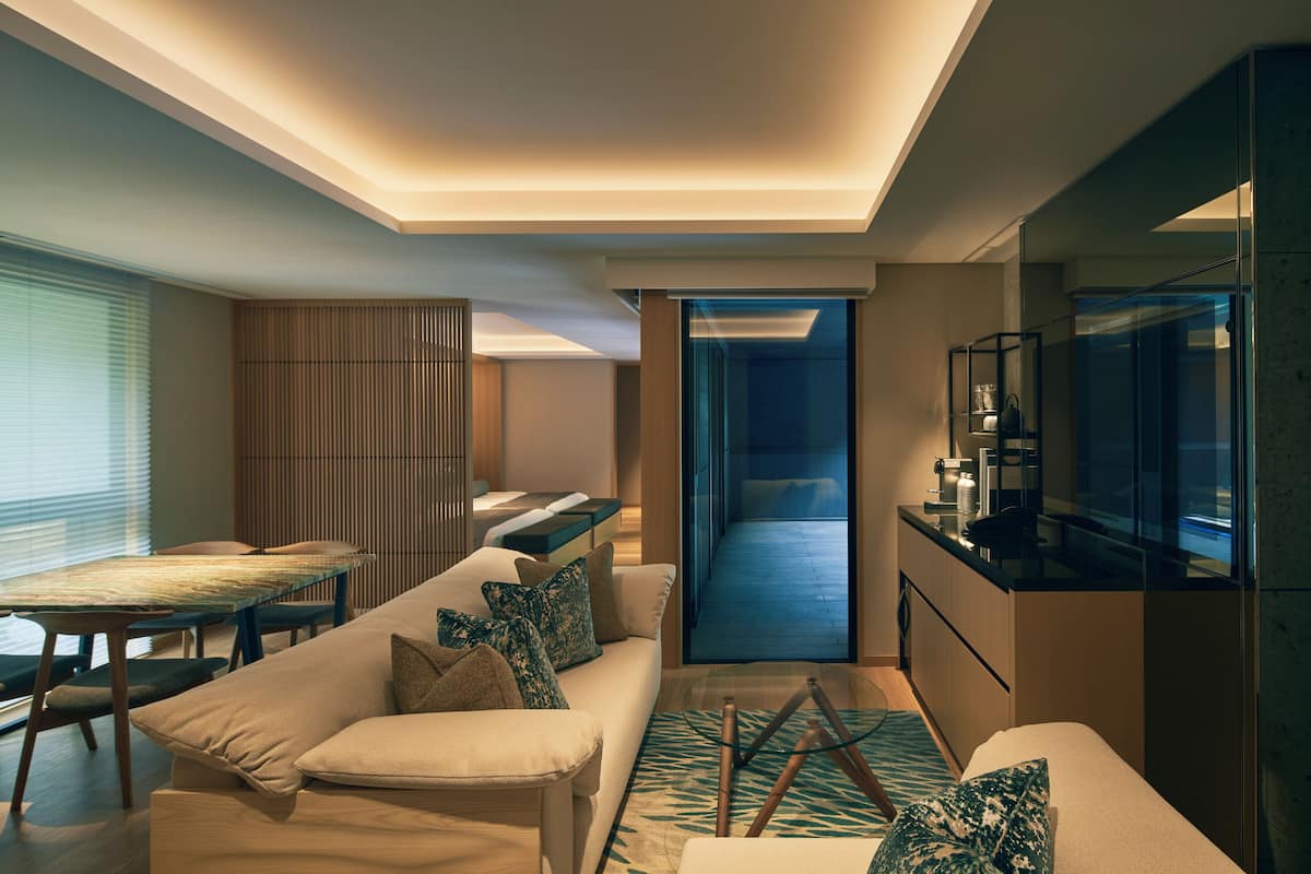 A modern hotel room with a sofa, dining table, and a TV.