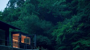 A modern building with a glass enclosure, surrounded by dense forest. - ESPACIO The Hakone Geihinkan Rin-Poh-Ki-Ryu (Hakone)