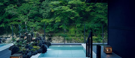 A serene outdoor hot tub area with a wooden deck, surrounded by lush greenery and rocks.