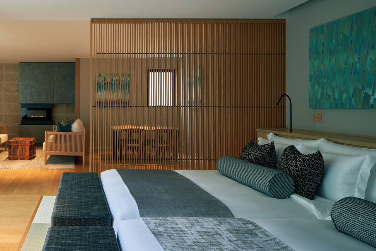 A modern hotel room with a large bed, a seating area with a table, and a large abstract painting on the wall.