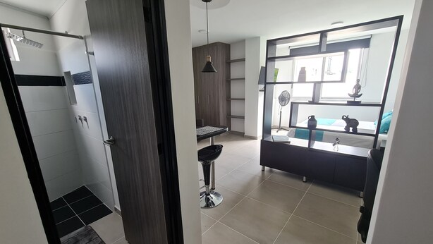 Un baño moderno con ducha, inodoro y lavamanos. Hay una puerta que da a otra habitación.