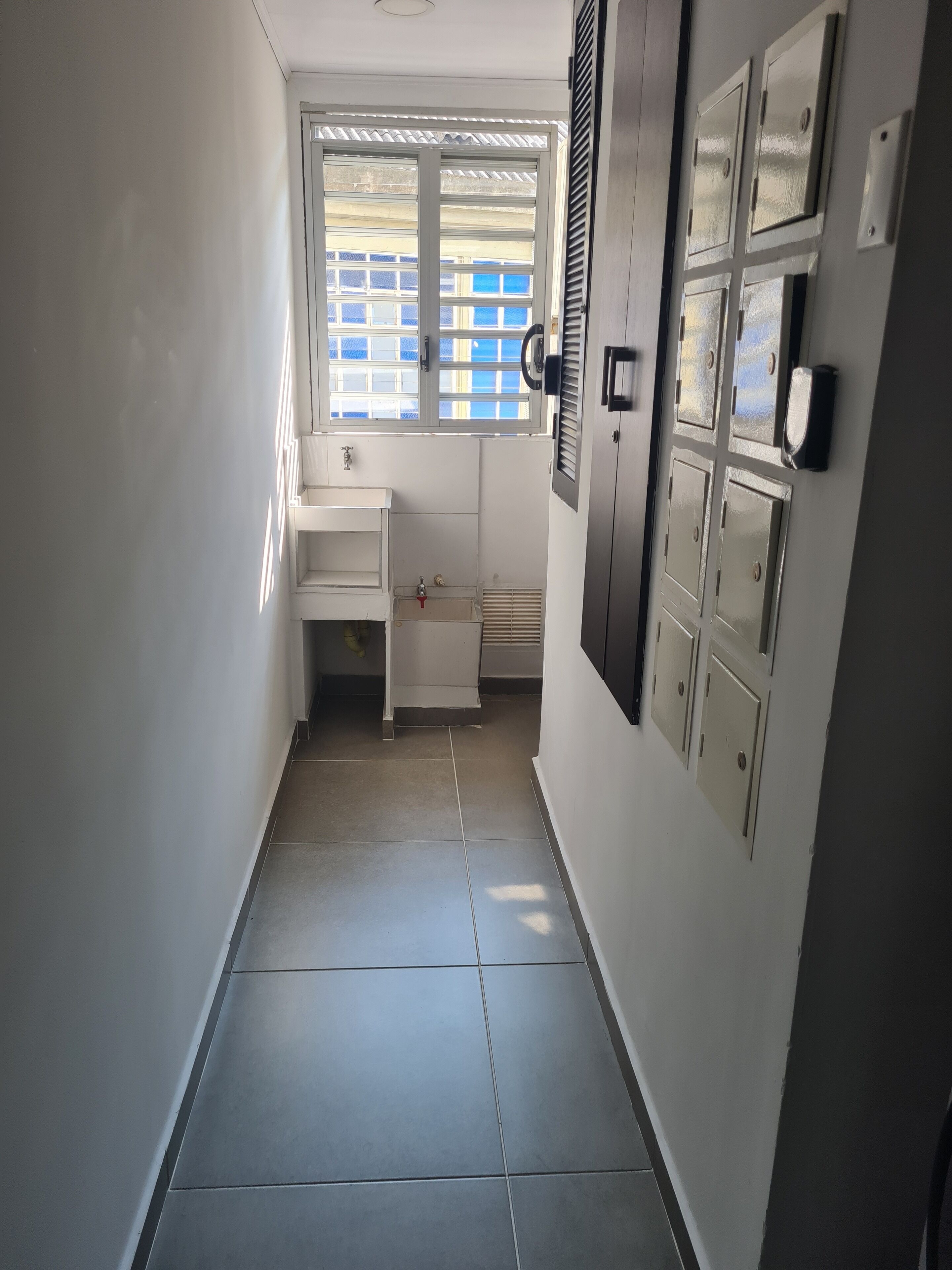 A narrow hallway with a window, a small sink, and a door with multiple locks.