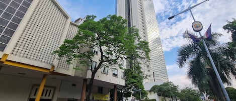 A street view with tall buildings, parked cars, and a clear sky.