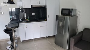 Cocina compacta con armarios blancos, encimera negra, refrigerador de acero inoxidable y microondas.