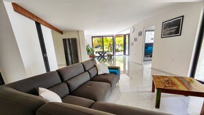 A modern living room with a large brown sofa, a wooden coffee table, and a view of the outdoors through large windows.