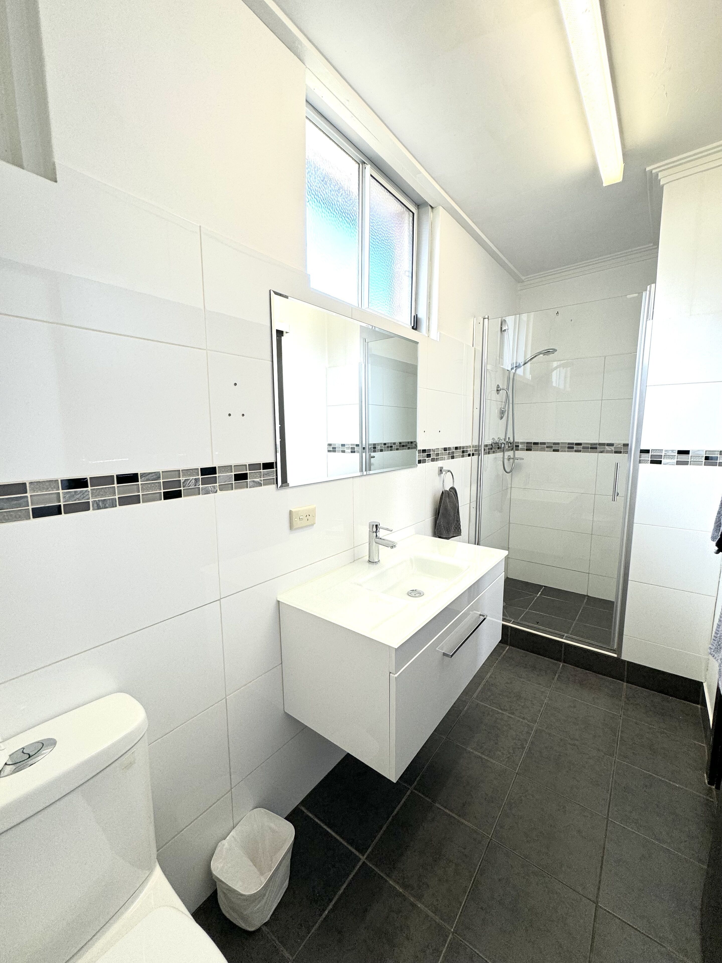 A modern bathroom with a white vanity, a glass shower enclosure, and a tiled floor.