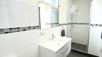 A modern bathroom with a white vanity, a glass shower enclosure, and a tiled floor.