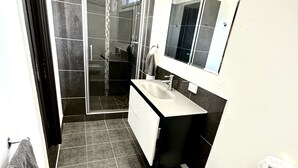 Un baño moderno con cabina de ducha de vidrio, lavamanos blanco y un espejo grande sobre el mueble.