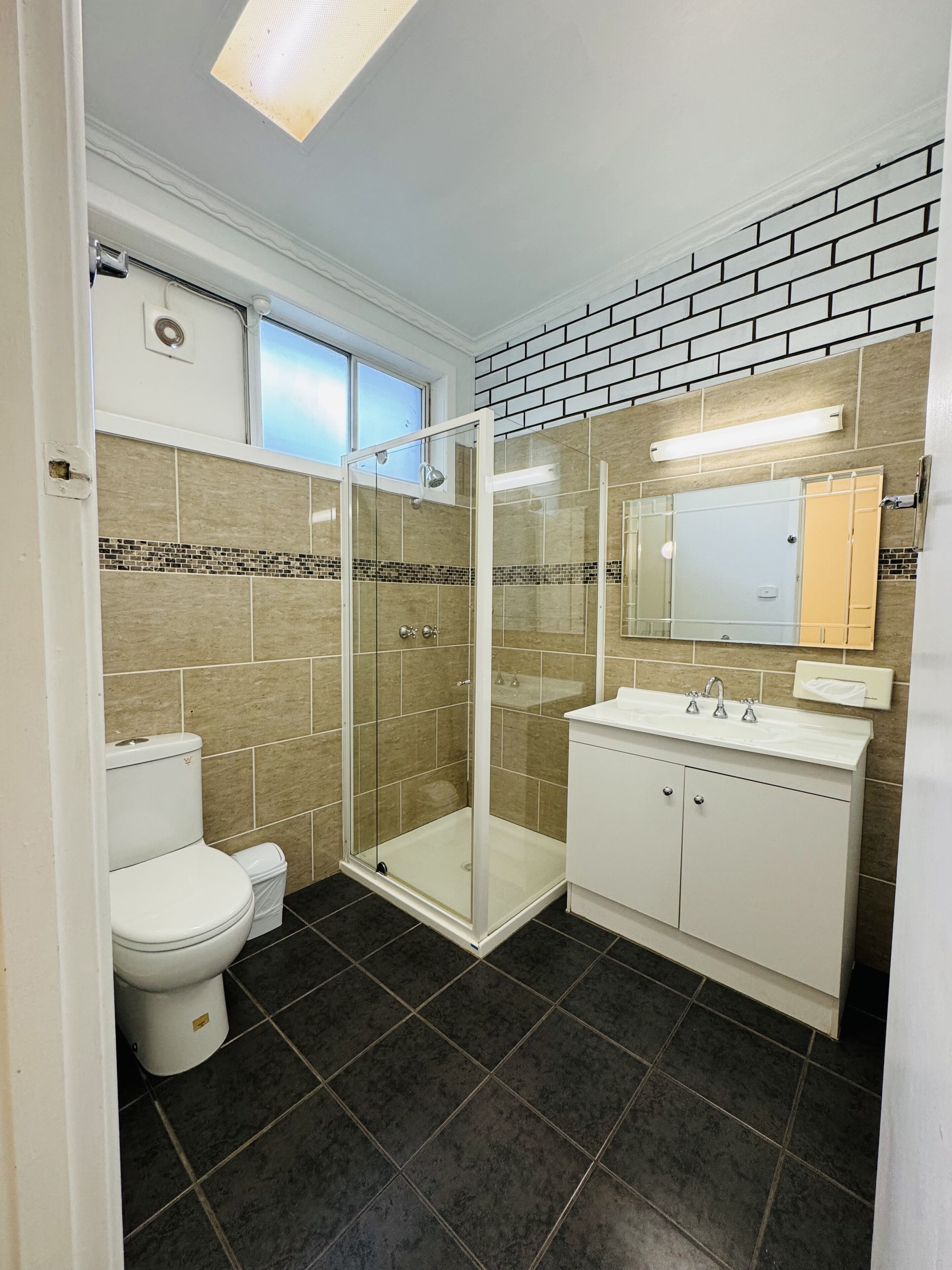 A bathroom with a glass-enclosed shower, a toilet, and a sink with a mirror above it.