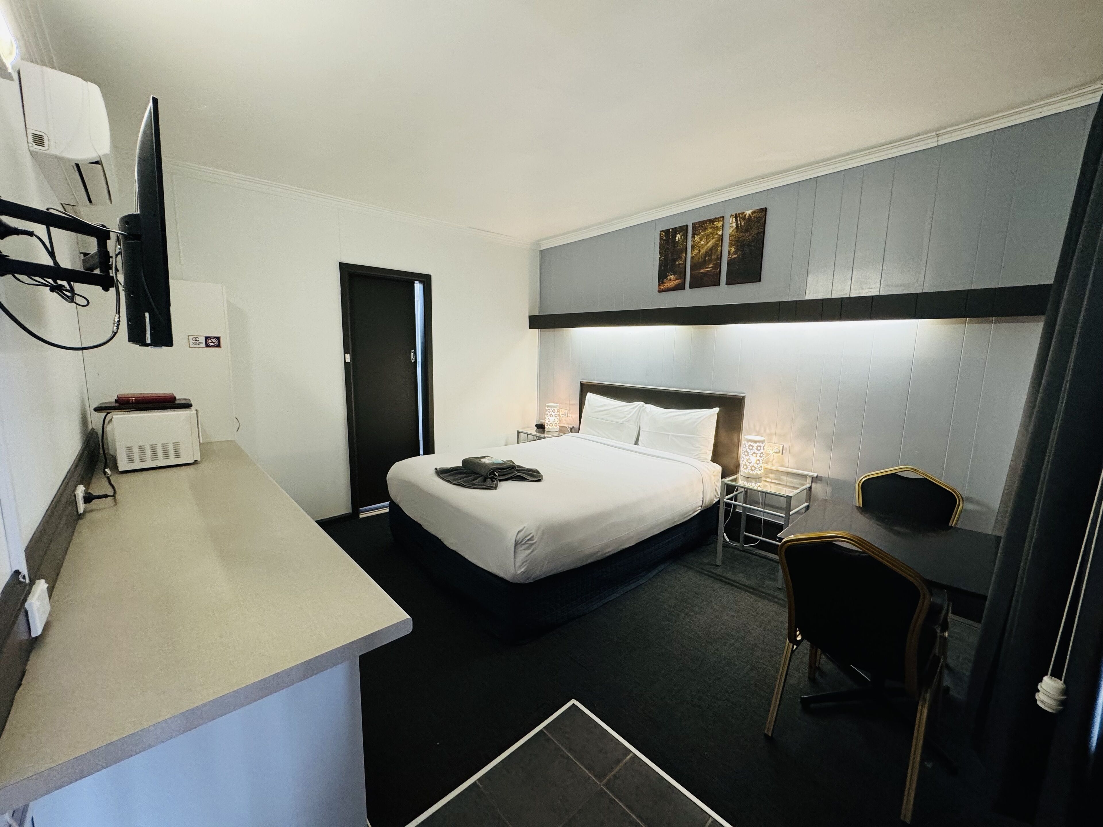 A hotel room with a bed, bedside table, desk, chair, and a television.