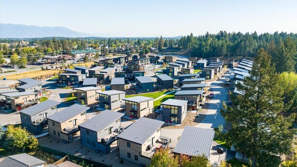 Un quartier résidentiel moderne caractérisé par des logements compacts, un espace vert central et un paysage de montagnes et de forêts en arrière-plan.