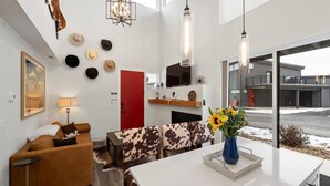 Un salon moderne avec un canapé en peau de vache, une porte rouge et une grande fenêtre donnant sur un immeuble.