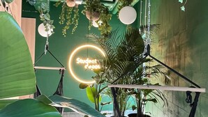Une pièce décorée de plantes suspendues, d’un hamac et d’un panneau lumineux au néon.