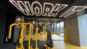 Une salle de sport avec un grand panneau néon sur lequel on peut lire « WORK IT » et divers appareils d’exercice.