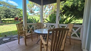 Eine überdachte Terrasse mit einem runden Tisch und vier Holzstühlen, umgeben von einem weißen Geländer, mit Blick auf eine gepflegte Rasenfläche und Bäume.